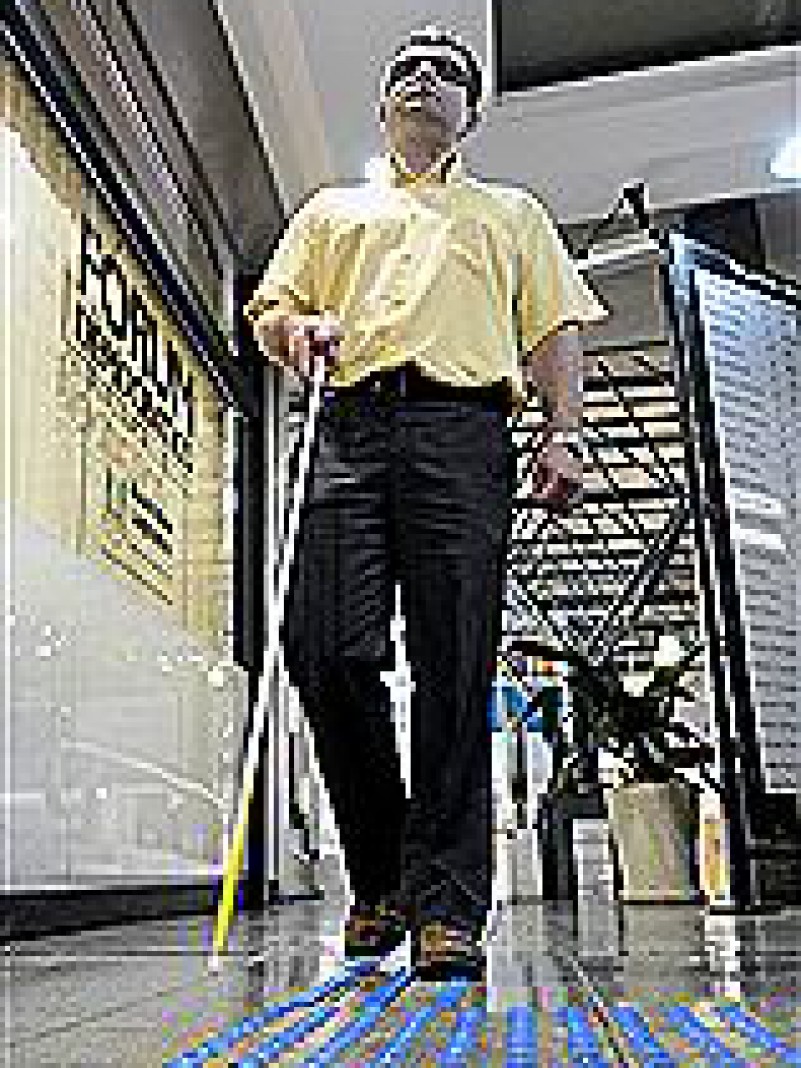 Pessoa cega, com bengala, entrando na Assembleia Legislativa do RS, sob piso táctil. Foto Divulgação.
