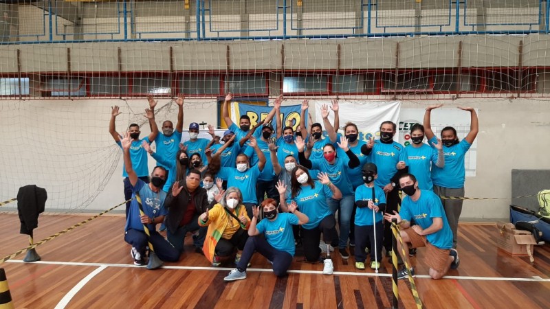 25 pessoas, com e sem deficiência, a maioria usando camiseta azul da Esporte Mais, todos com máscaras de proteção facial, acenam para a foto.
