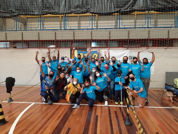 25 pessoas, com e sem deficiência, a maioria usando camiseta azul da Esporte Mais, todos com máscaras de proteção facial, acenam para a foto.