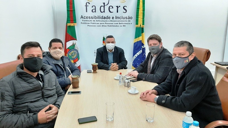 Cinco homens, todos sentados ao redor de uma mesa retangular e usando máscaras de proteção facial, posam para a foto. Ao fundo, o banner da FADERS Acessibilidade e Inclusão.