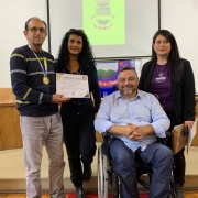 Sentado em cadeira de rodas, o presidente da FADERS posa para a foto entre um homem e duas mulheres em pé. O homem segura um certificado de participação no Praia Acessível.