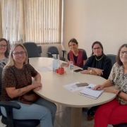 Foto: paredes em tom de um pessego placo, mesa com tampa bege clara madeira e cadeiras com encostos pretos ao redor, nelas a vereadora de Bagé, Ana Paula da Silva Moreira, a assessora jurídica Marília Scardoelli dos Santos, a assessora parlamentar Maíra Zago e a intérprete de Libras Renata de Melo Machado, todas de Bagé, e a coordenadora de acessibilidade da Faders, Jaqueline Rosa 
