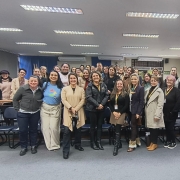 Foto ambiente interno, parece claras cortinas azuis, carpete cinza no ch&atilde;o, cadeiras pretas e em primeiro plano os participantes da oficina posam para foto com as ministrantes das atividades - servidoras da Faders 
